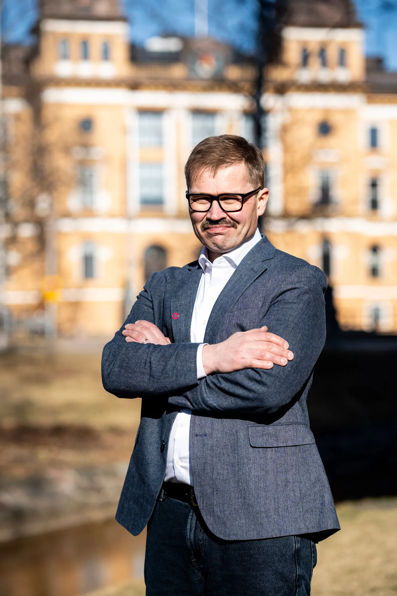 Olli Kohonen kädet ristissä Oulun kaupungintalon edessä aurinkoisena päivänä.