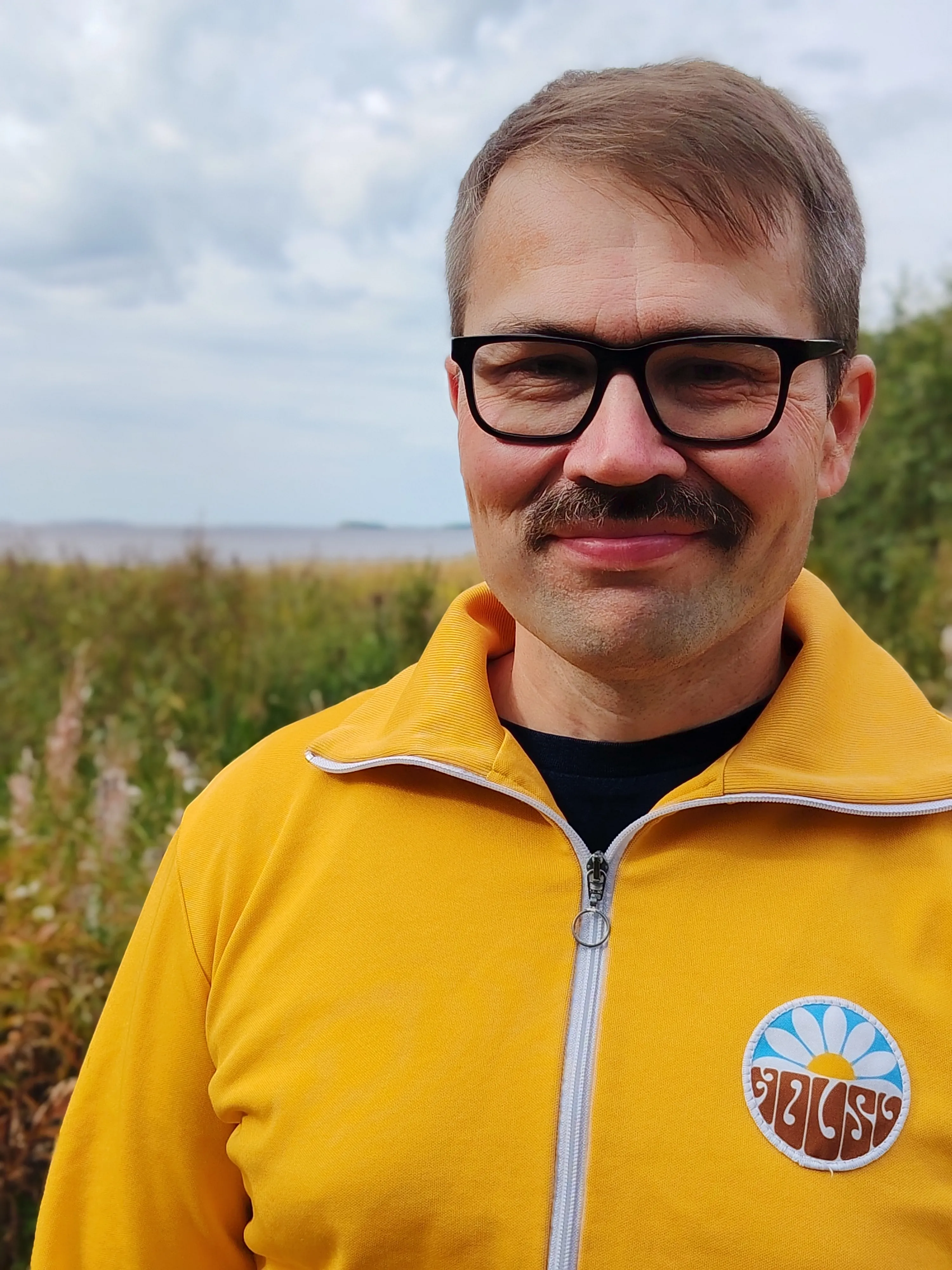 Olli Kohonen hymyilee keltaisessa verryttelytakissa Perämeren rannalla.